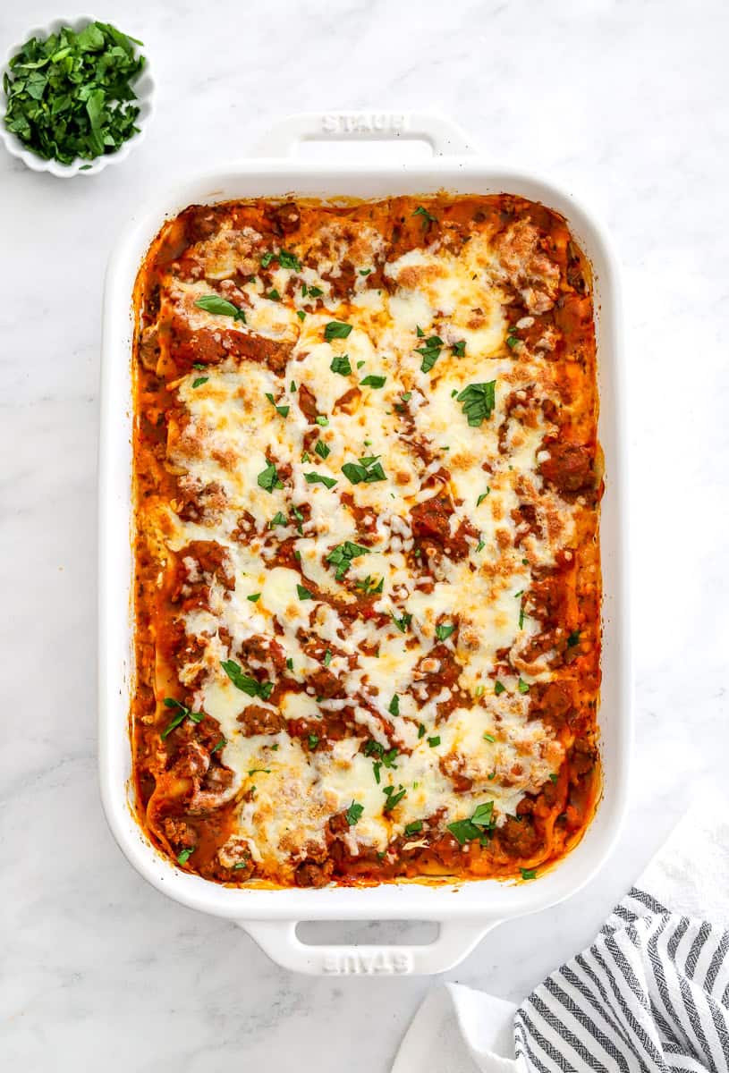 Baked lasagna with melty cheese on top with a stripped towel next to it.