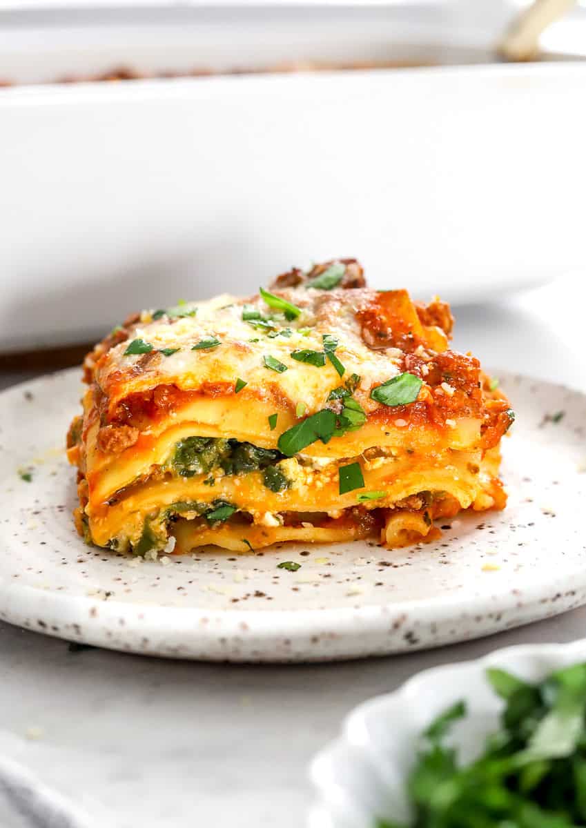 Slice of cottage cheese lasagna on a plate with a pan of it behind it.