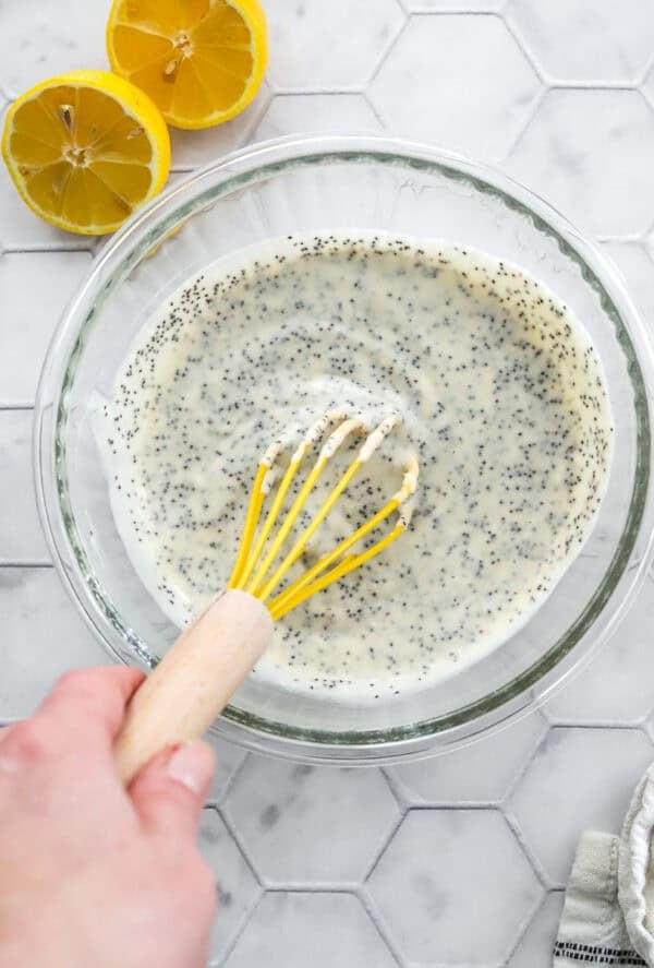 Mixing poppyseed dressing in a glass bowl with a yellow whisk.