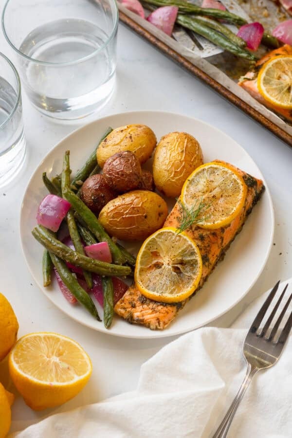 Plate of sheet pan salmon meal with more on the pan behind it.