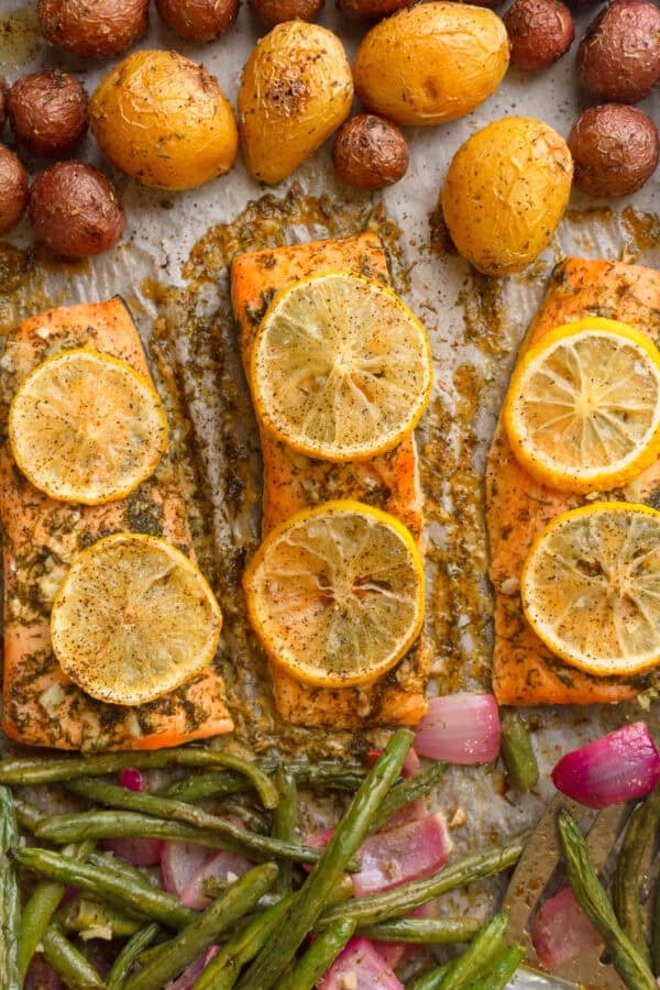 Sheet pan salmon with green beans and potatoes cooked on a baking pan with lemon slices on the salmon filets.