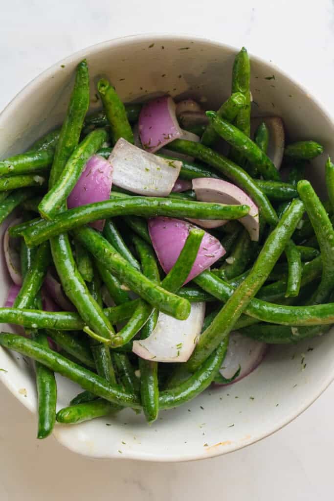 Marinated green beans and onion in a white bowl. 