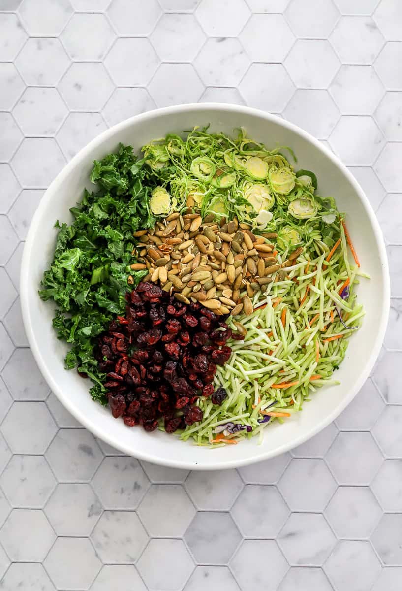 Kale slaw salad in a bowl with dried cranberries, pepitas and shaved Brussels sprouts.