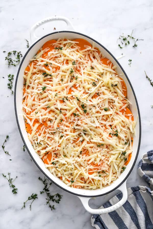 unbaked, layered sweet potato gratin with cheese on top in an oval pan.