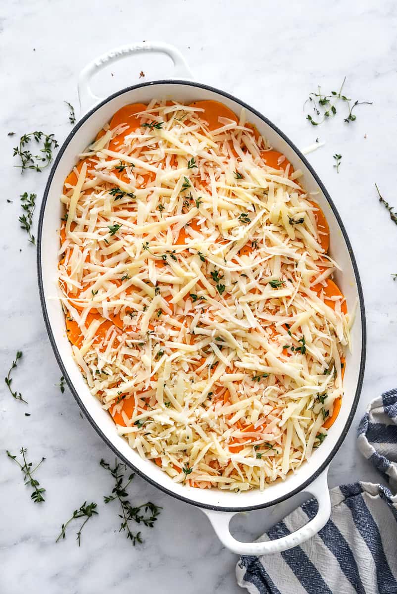 unbaked, layered sweet potato gratin with cheese on top in an oval pan. 