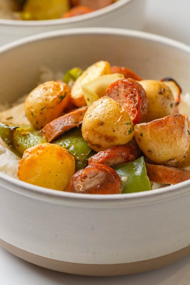 Golden air fried potatoes, peppers and sausage over rice in a bowl with another bowl behind it. 
