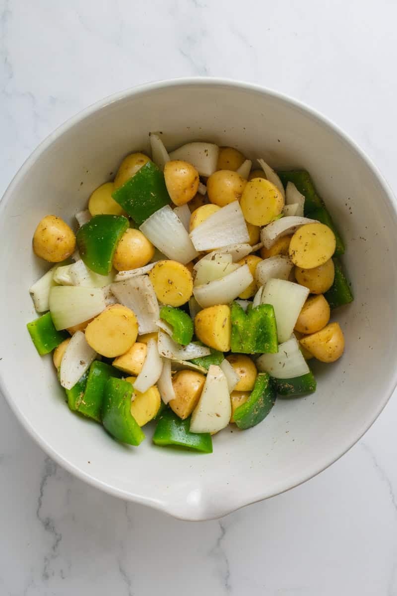Chopped green bell pepper, onion and baby gold potatoes in a ceramic mixing bowl. 