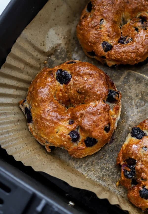 Blueberry bagel cooked in an air fryer basket with more around it.