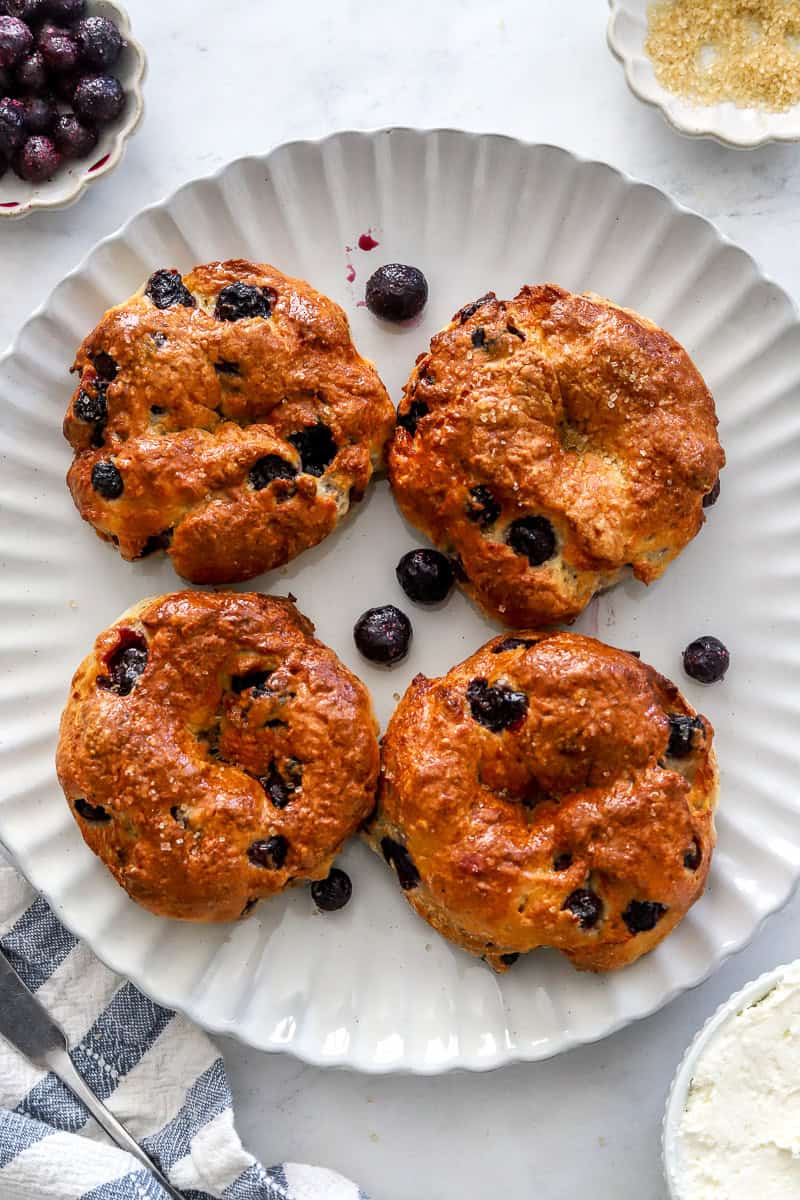 Blueberry bagels on a plate with cream cheese and a striped towel in front of it.