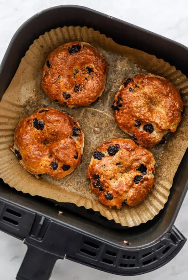 Cooked blueberry bagels in an air fryer basket.