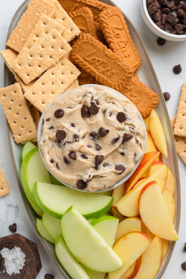 Platter with a bowl of cottage cheese cookie dough in the center with apple slices, graham crackers and biscoff cookies around it on the platter.