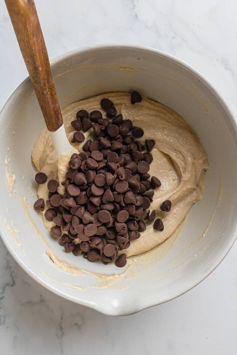 Cottage cheese cookie dough in a mixing bowl with a pile of chocolate chips on it.