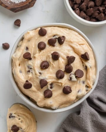 Round bowl filled with no bake cottage cheese cookie dough with chocolate chips with a grey towel next to it.