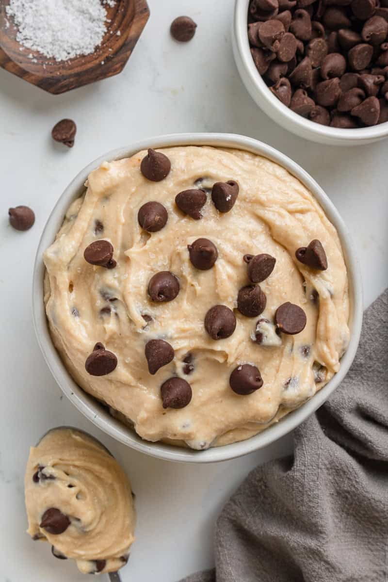 Round bowl filled with no bake cottage cheese cookie dough with chocolate chips with a grey towel next to it.