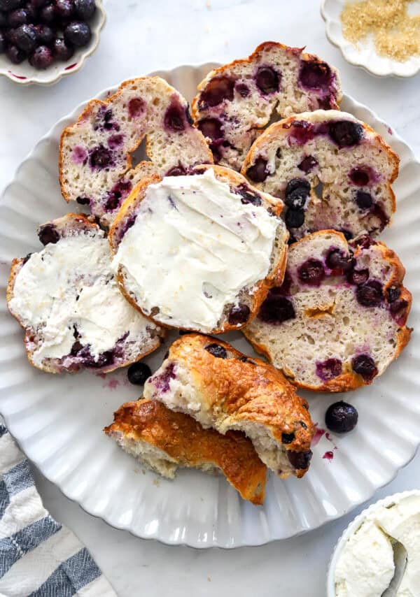 Plate filled with sliced Geek yogurt blueberry bagels with cream cheese spread on a couple of them.