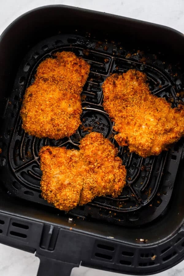 3 pieces of cooked crispy breaded chicken in a black air fryer basket.