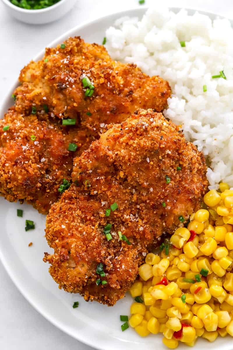 Crispy air fried chicken thighs on a plate with some corn and rice, topped with chopped herbs.