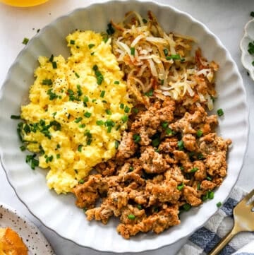 High protein breakfast bowl with scrabbled eggs and cooked ground meat with shredded golden potatoes in a bowl.