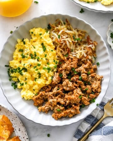High protein breakfast bowl with scrabbled eggs and cooked ground meat with shredded golden potatoes in a bowl.