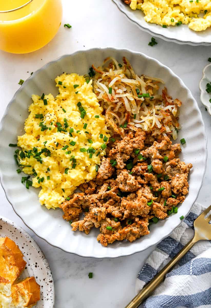High protein breakfast bowl with scrabbled eggs and cooked ground meat with shredded golden potatoes in a bowl.