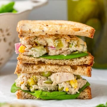 Matthew MCconaughey tuna salad between bread as a stacked sandwich with a jar of pickles behind it.
