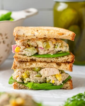 Matthew MCconaughey tuna salad between bread as a stacked sandwich with a jar of pickles behind it.