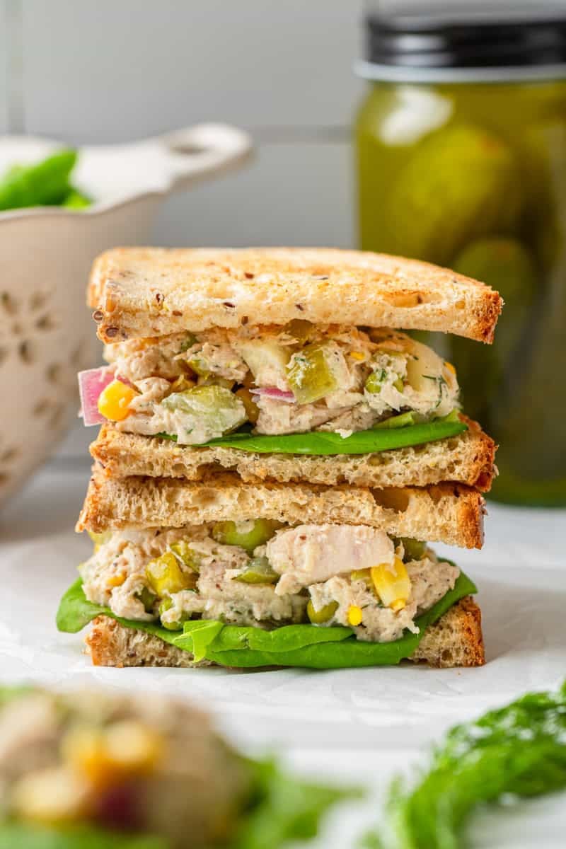 Matthew MCconaughey tuna salad between bread as a stacked sandwich with a jar of pickles behind it. 