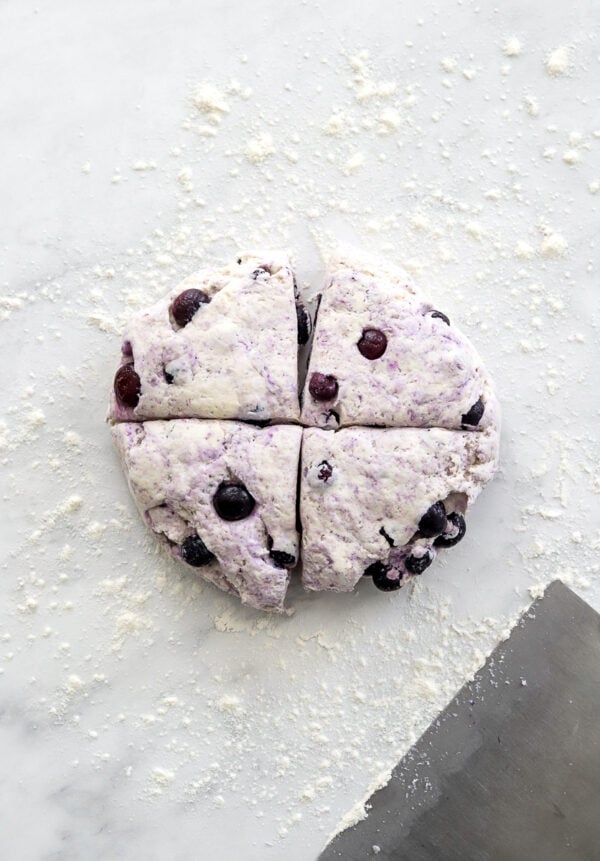 Portioned blueberry bagel dough on a floured surface with a metal cutter in front of it.