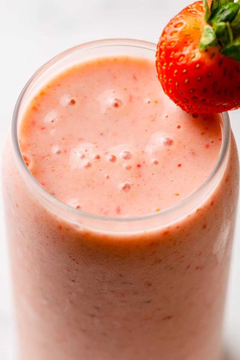 Glass filled with strawberry smoothie with a whole strawberry on the side of the glass. 