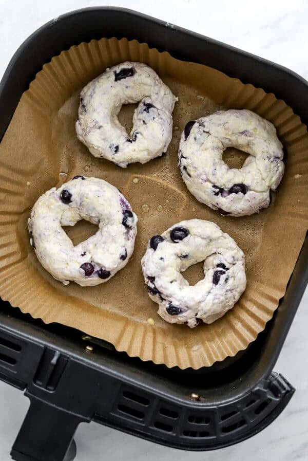 Uncooked bagels in an air fryer basket.