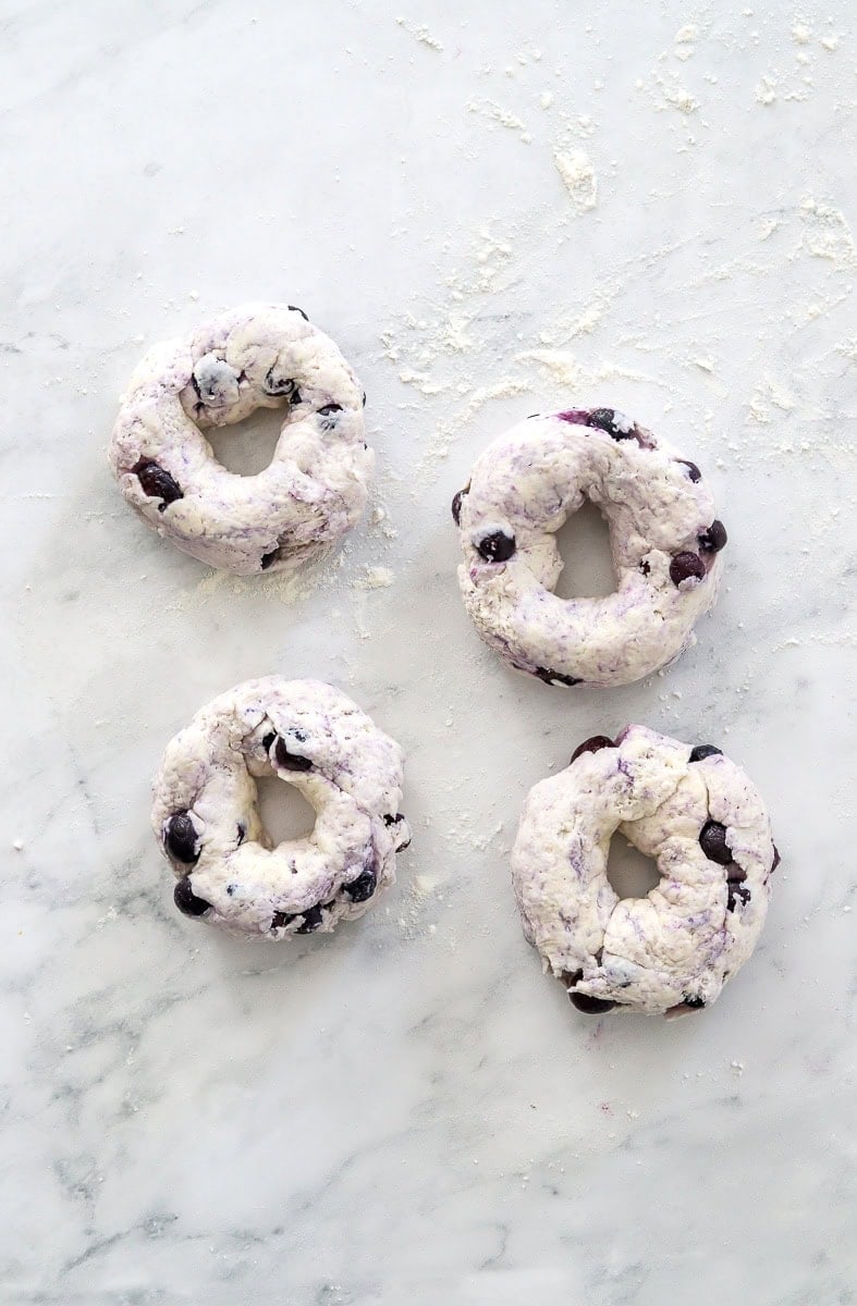 Uncooked blueberry yogurt bagels formed on a marble surface.