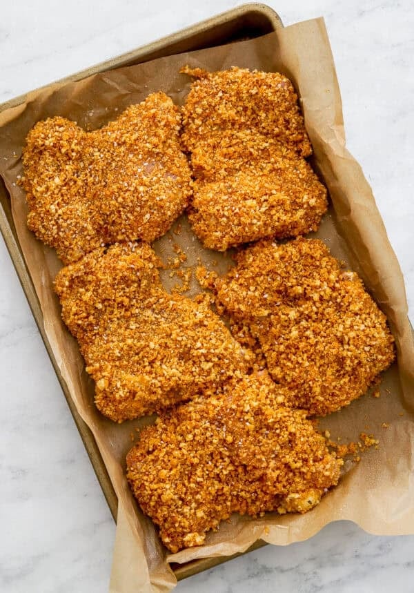 Uncooked coated chicken thighs on a parchment paper lined pan.