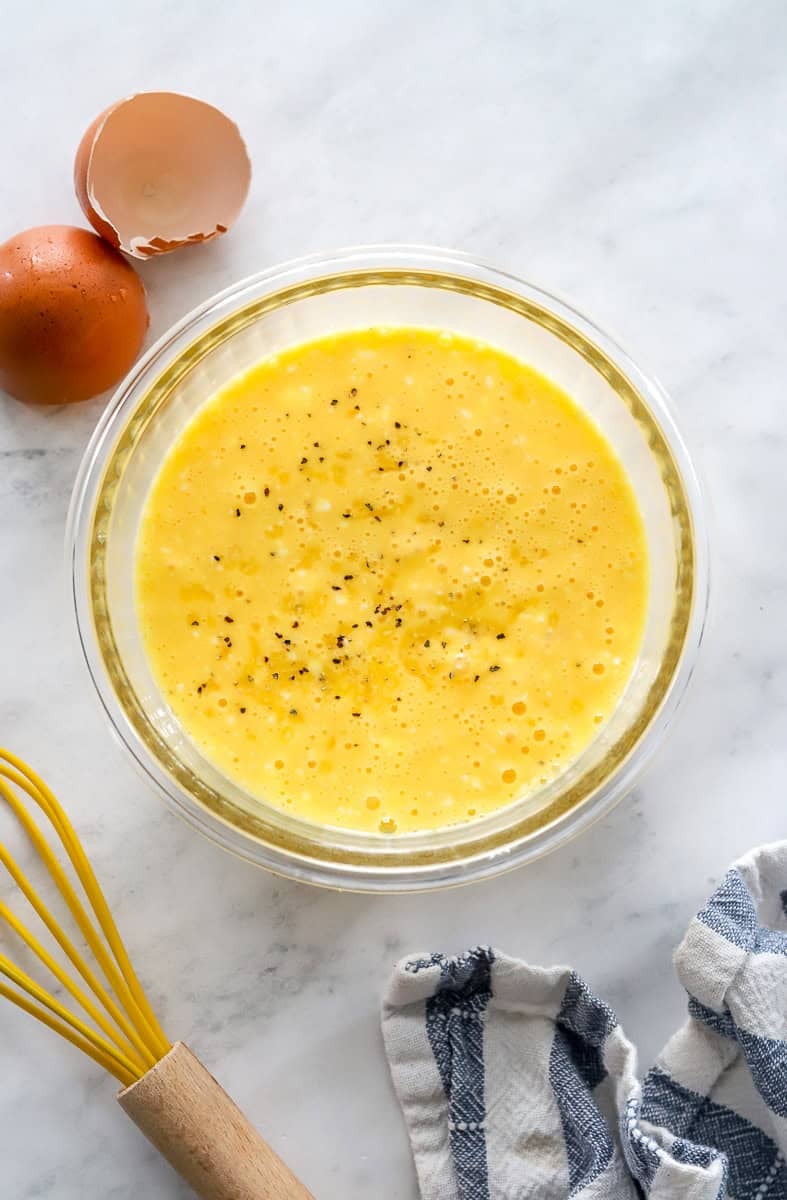 Whisked eggs and cottage cheese in a glass bowl with a yellow whisk in front of it.