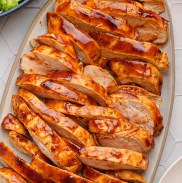 Platter of air fryer bbq chicken breast sliced with salad in a bowl behind it.