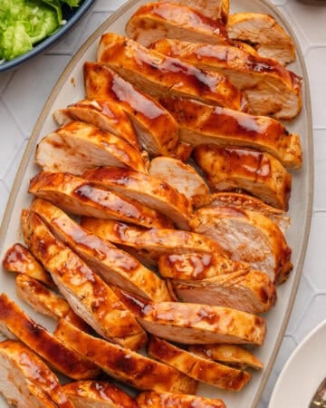 Platter of air fryer bbq chicken breast sliced with salad in a bowl behind it.
