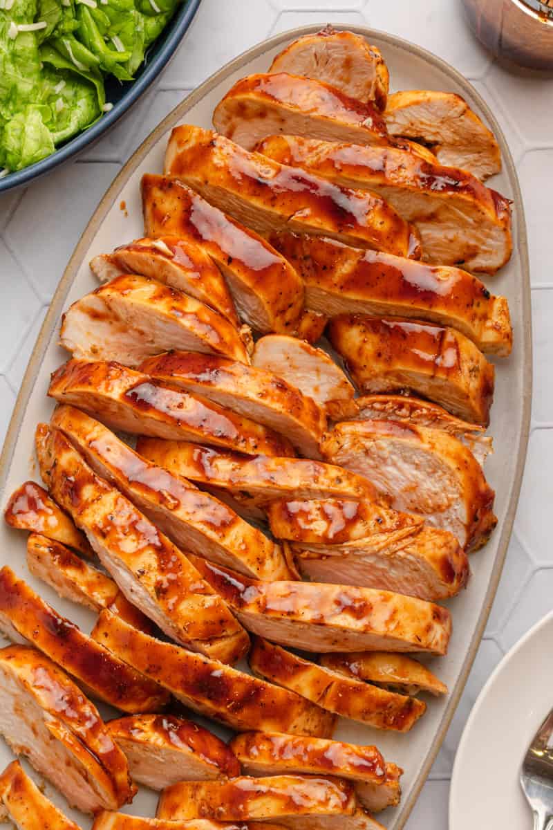 Platter of air fryer bbq chicken breast sliced with salad in a bowl behind it.
