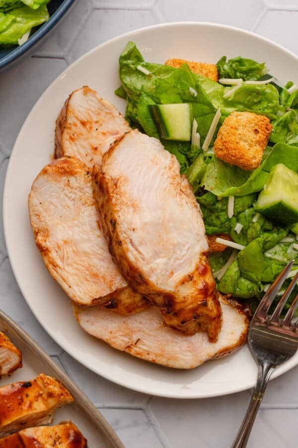 Cooked slices of air fried chicken with bbq sauce on a plate with some salad.