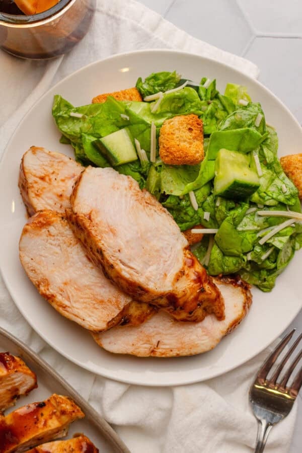 Air fryer chicken breast with bbq sauce on a plate with some salad with more infant of it.