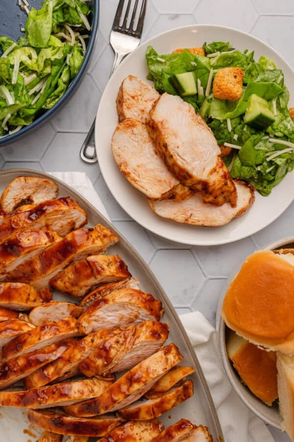 Cooked bbq chicken with some on plate sliced and some on a plate with some salad next to it.