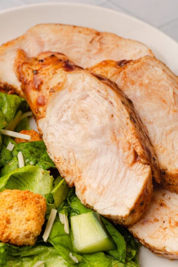 Cooked sliced bbq chicken breast on a plate on top of a salad.
