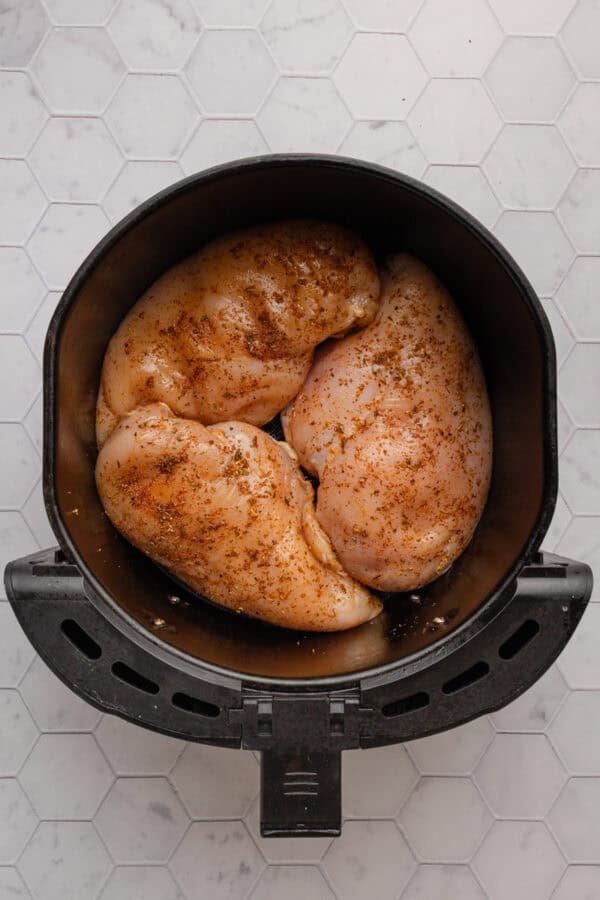 Uncooked, seasoned chicken breast in round air fryer basket.