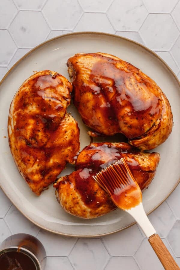 White brush brushing bbq sauce on air fried chicken breast.