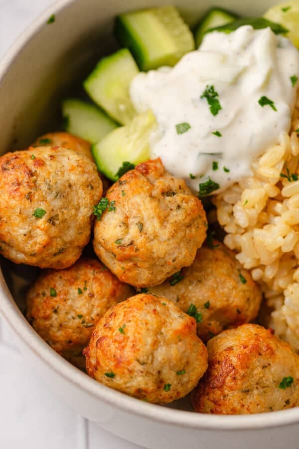 Cooked lean meatballs in a bowl with brown rice, zucchini and some tzatziki.