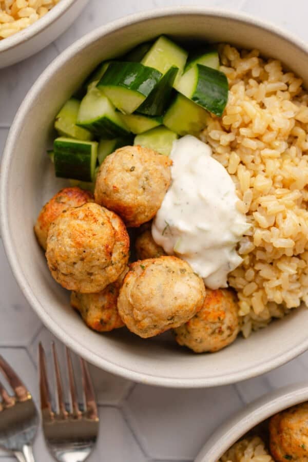 Golden cooked meatballs in a bowl with rice zucchini and tzatziki sauce.