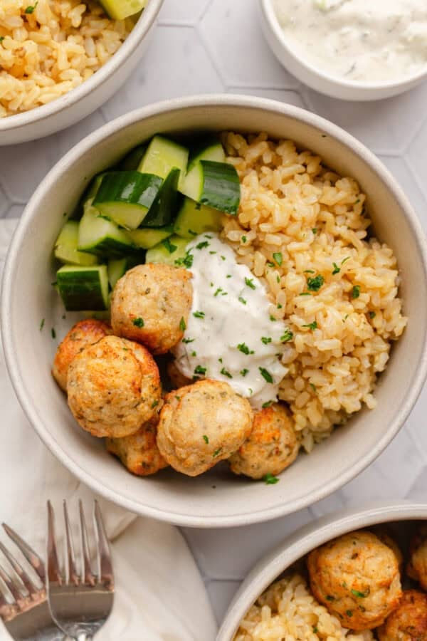 Round bowl filled with air fryer chicken meatballs with cooked brown rice and zucchini in the bowl with it with more bowls of it around it.
