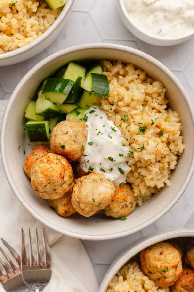 Round bowl filled with air fryer chicken meatballs with cooked brown rice and zucchini in the bowl with it with more bowls of it around it.
