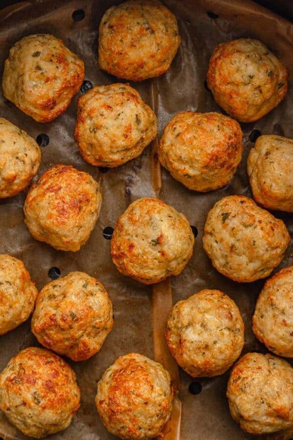 Close up of cooked meatballs in lined air fryer basket.