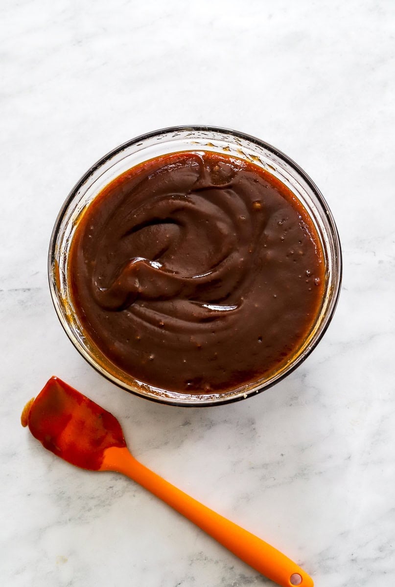 Glass bowl filled with BBQ sauce with an orange spatula next to it. 