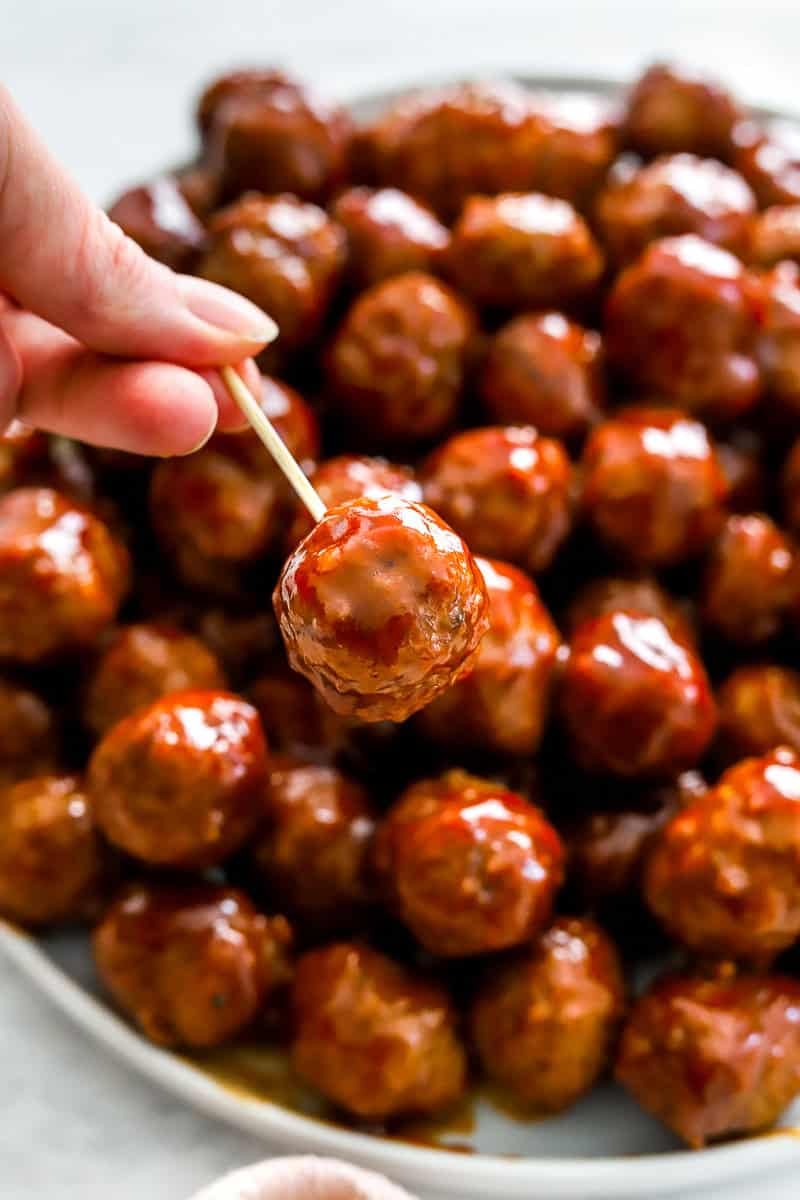 Plate of 3 ingredient meatballs with a hand holding one with a toothpick. 