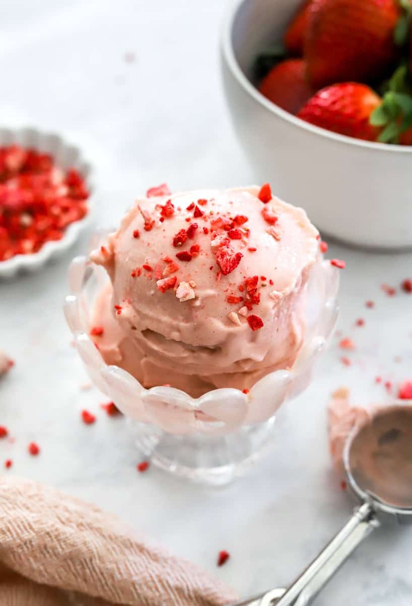 Glass ice cream dish with scooped strawberry protein ice cream in it topped with freeze dried strawberries. 